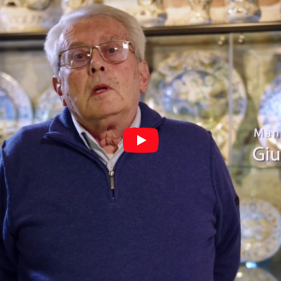 Giuseppe Matricardi mentre parla, alle sue spalle la collezione di piatti all'interno di una teca in vetro illuminata.