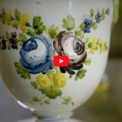 Vaso bianco con decorazione della rosa dei Paci, due rose una blu e una marrone con foglie verdi e fiorellini gialli, marroni e blu.